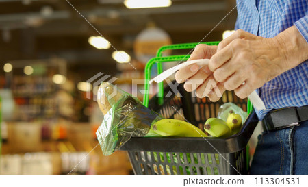 A grocery receipt in the hands of an older man 113304531