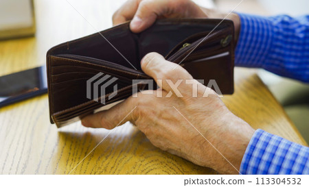 An empty wallet with no money in the hand of an elderly white man about to place an order at a cafe An empty wallet with no money in the hand of an elderly white man about to place an order at a cafe 113304532