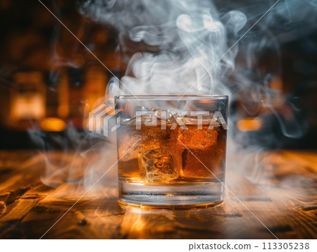 Glass of amber liquid with ice cubes on dark wooden table with blurred warm lights in the background Glass of amber liquid with ice cubes on dark wooden table with blurred warm lights in the background 113305238