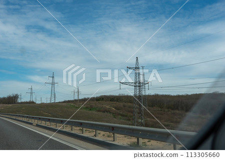 A road with a power line running along it. The sky is blue and there are some clouds 113305660