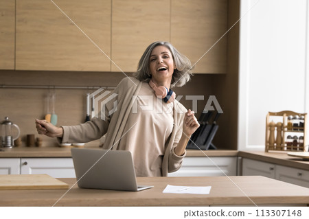 Happy mature woman enjoying music in kitchen at home 113307148