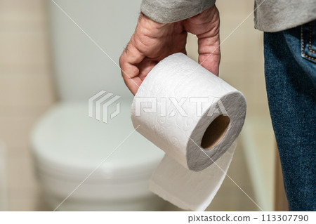An older man's hand holding a roll of toilet paper in front of the toilet. An older man's hand holding a roll of toilet paper in front of the toilet. 113307790