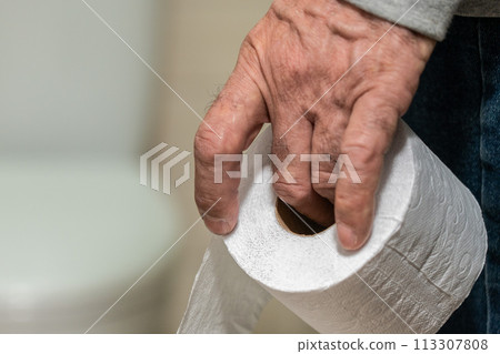 An older man's hand holding a roll of toilet paper in front of the toilet. An older man's hand holding a roll of toilet paper in front of the toilet. 113307808