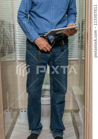 An older man in jeans and a shirt is standing over the toilet holding a clipboard. 113307811