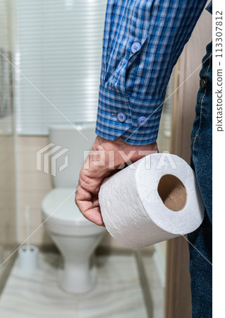 An older man's hand holding a roll of toilet paper in front of the toilet. 113307812
