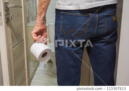 An older man's hand holding a roll of toilet paper in front of the toilet. 113307813