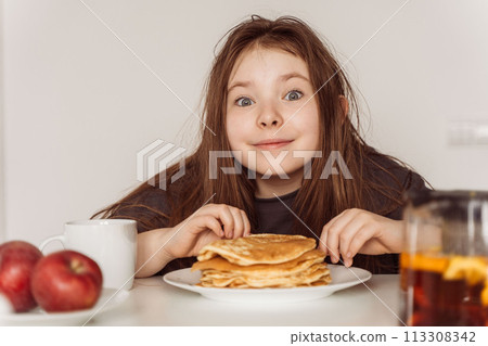 Little cheerful teenage girl preparing to eat a stack of pancakes for breakfast. High quality photo Little cheerful teenage girl preparing to eat a stack of pancakes for breakfast. High quality photo 113308342