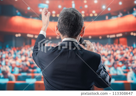 Man speaking in front of a large audience 113308647