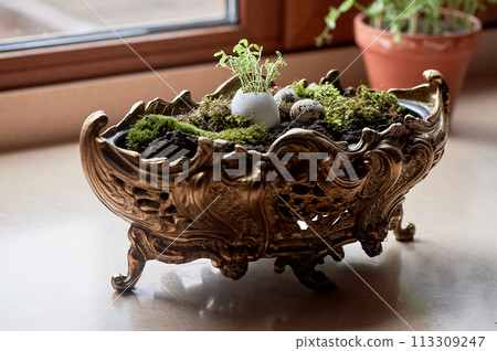 A massive bronze vase on legs with moss, greenery sprouted in an egg. A new life 113309247