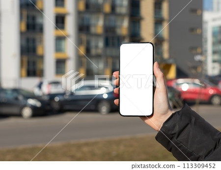 Hand holding mobile phone screen mockup, empty blank smartphone, cars and city buildings 113309452