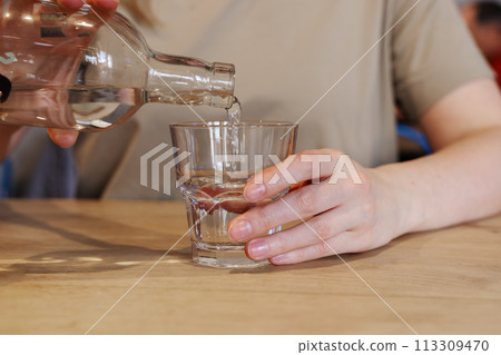Hand pouring water from bottle into glass at wooden table Hand pouring water from bottle into glass at wooden table 113309470