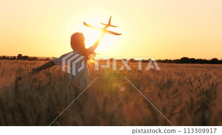 Adorable female kid silhouette running with aircraft toy at cinematic sunset sunrise wheat field back view. Happy little girl child playing pilot game with plane plaything enjoy childhood at dusk Adorable female kid silhouette running with aircraft toy at cinematic sunset sunrise wheat field back view. Happy little girl child playing pilot game with plane plaything enjoy childhood at dusk 113309917