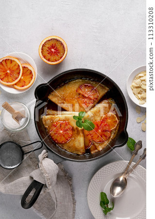 Crepes with Orange Sauce in a cast iron pan. Traditional French crepe Suzette with orange sauce. Flat lay, top view, copy space Crepes with Orange Sauce in a cast iron pan. Traditional French crepe Suzette with orange sauce. Flat lay, top view, copy space 113310208