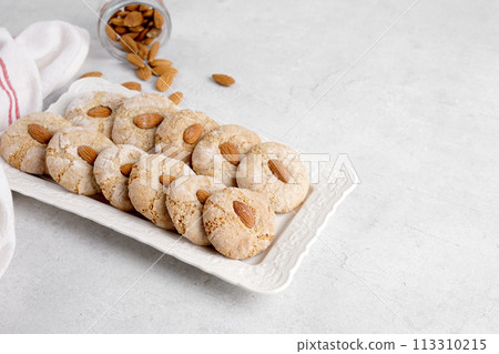 Italian almond cookies coated in powdered sugar, delicious biscuits styled in ceramic plate with napkin, paste di mandorle, copy space 113310215