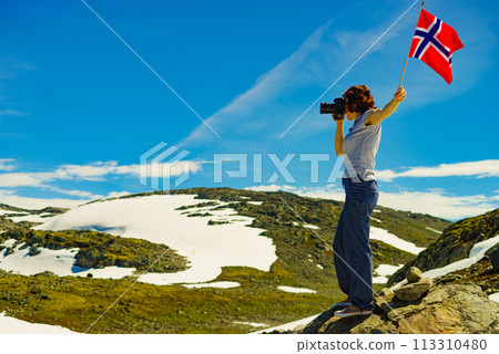 Tourist holds camera and norwegian flag in mountains Tourist holds camera and norwegian flag in mountains 113310480