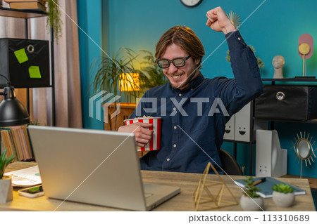 Business man taking break from work wearing 3D glasses eating popcorn and watching movie at office 113310689
