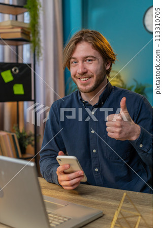 Smiling businessman using smartphone app online pointing showing like thumbs up remote distance job Smiling businessman using smartphone app online pointing showing like thumbs up remote distance job 113310705