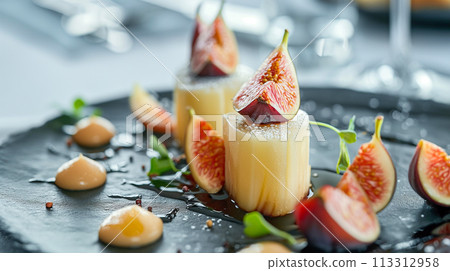 A gourmet panna cotta dessert garnished with fresh fig slices and served with a rich berry coulis. 113312958
