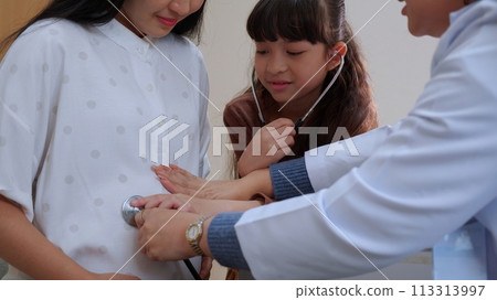 Asian daughter using stethoscope listening baby heartbeat with mother while doctor by side. 113313997