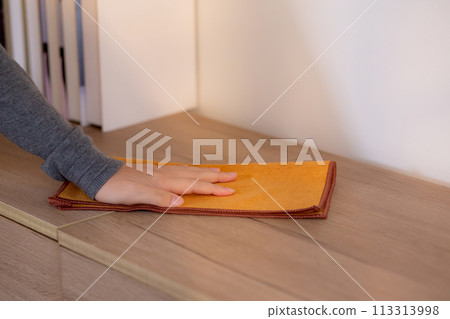 Closeup hand young asian woman wearing apron cleaning and dusting polishing on wooden cabinet. 113313998
