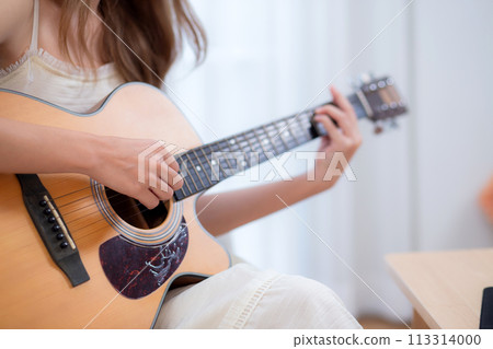 Closeup hands of young asian woman sitting on sofa playing guitar in living room at home. Closeup hands of young asian woman sitting on sofa playing guitar in living room at home. 113314000