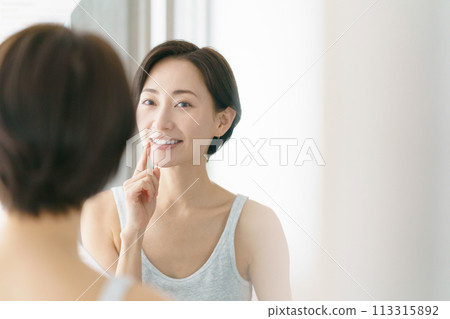中年婦女對著鏡子檢查牙齒 中年婦女對著鏡子檢查牙齒 113315892