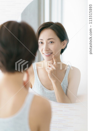 Middle-aged woman checking her teeth in the mirror Middle-aged woman checking her teeth in the mirror 113315893