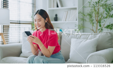 Happy young asian woman relax on comfortable couch at home texting messaging on smartphone Happy young asian woman relax on comfortable couch at home texting messaging on smartphone 113316526