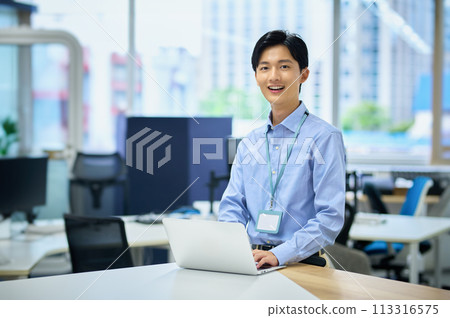 A young male businessman in casual clothes operating a computer in an office 113316575