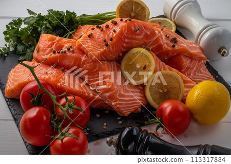 Fresh raw salmon fillet with cooking ingredients, herbs and lemon on black slate Fresh raw salmon fillet with cooking ingredients, herbs and lemon on black slate 113317884