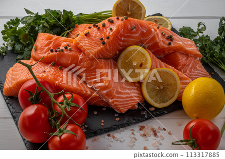 Fresh raw salmon fillet with cooking ingredients, herbs and lemon on black slate Fresh raw salmon fillet with cooking ingredients, herbs and lemon on black slate 113317885