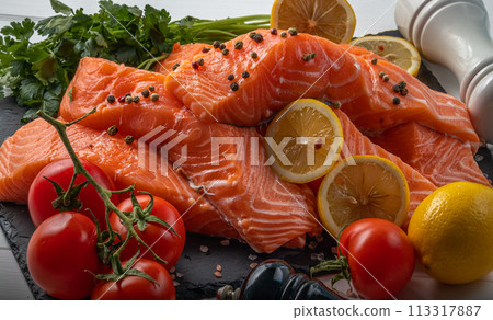 Fresh raw salmon fillet with cooking ingredients, herbs and lemon on black slate 113317887