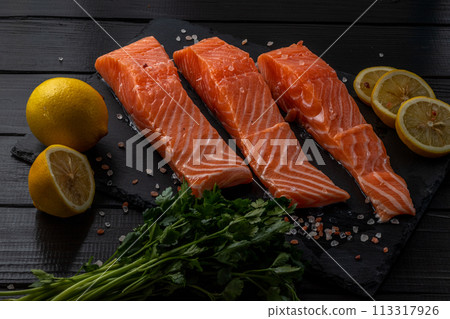 Fresh raw salmon fillet with cooking ingredients, herbs and lemon on black slate Fresh raw salmon fillet with cooking ingredients, herbs and lemon on black slate 113317926