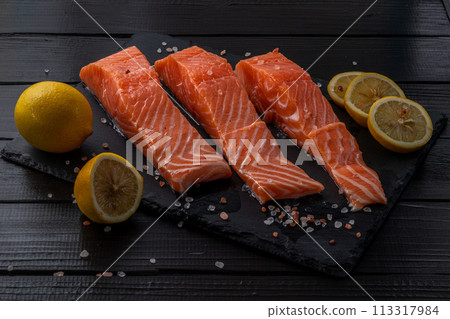 Fresh raw salmon fillet with cooking ingredients, herbs and lemon on black slate Fresh raw salmon fillet with cooking ingredients, herbs and lemon on black slate 113317984
