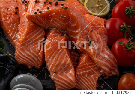 Fresh raw salmon fillet with cooking ingredients, herbs and lemon on black slate 113317985
