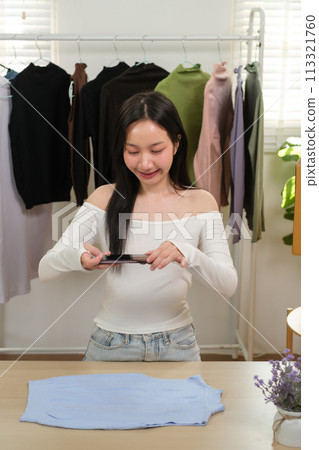 Young business woman takes a photo of a cloth with her smartphone device to put it up for sale on a second-hand clothing platform. online selling concept Young business woman takes a photo of a cloth with her smartphone device to put it up for sale on a second-hand clothing platform. online selling concept 113321760