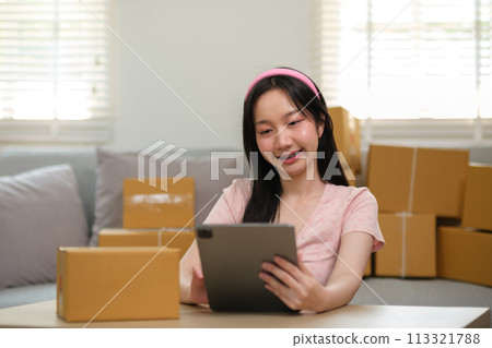 Asian business woman on sofa using a tablet checking customer order online shipping boxes at home. Starting SME Small business entrepreneur freelance. Online business, SME Work home concept. 113321788