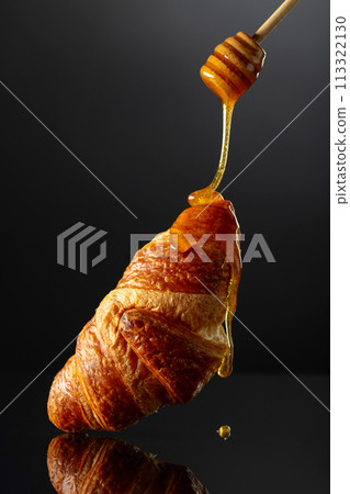 Fresh baked croissant with honey on a black background. Fresh baked croissant with honey on a black background. 113322130