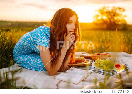 Young woman sits on a plaid with a book. Summer picnic in nature. Healthy food. Young woman sits on a plaid with a book. Summer picnic in nature. Healthy food. 113322390