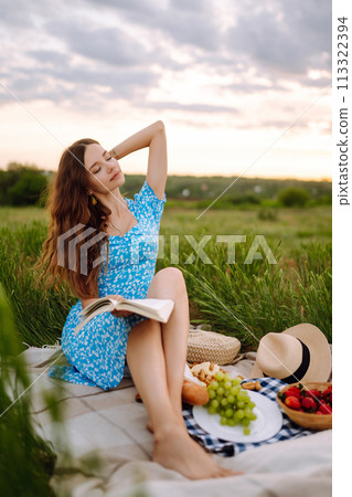 Young woman sits on a plaid with a book. Summer picnic in nature. Healthy food. Young woman sits on a plaid with a book. Summer picnic in nature. Healthy food. 113322394