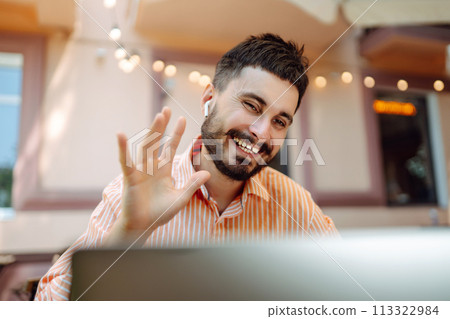 Happy male freelancer smiling while working at laptop with phone, online conference. Blog concept. 113322984