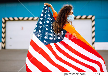 African American woman with medical face mask posing with american flag.The concept of preventing the spread of the epidemic. Covid-2019. 113323118