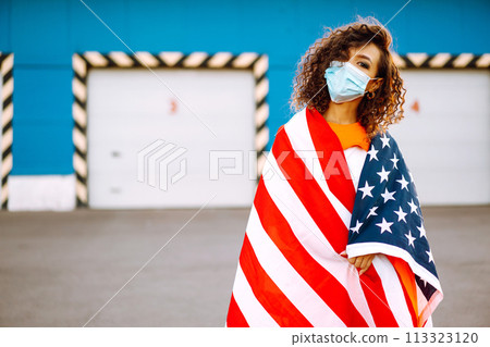 African American woman with medical face mask posing with american flag.The concept of preventing the spread of the epidemic. Covid-2019. 113323120