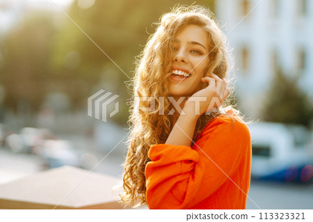 Young woman posing against backdrop of urban landscape in bright orange dress. Concept of lifestyle. Young woman posing against backdrop of urban landscape in bright orange dress. Concept of lifestyle. 113323321