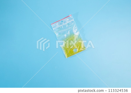 minimalism, featuring a plastic bag placed delicately on a blue surface. From the top view, the yellow liquid , part of crafting process 113324536
