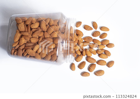 Almonds falling from a glass container leaning against a white background 113324824