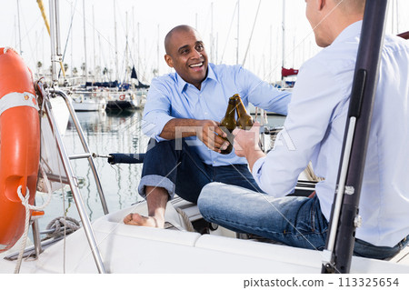 Couple of guys in blue shirts and jeans are chatting on a private yacht in the port Couple of guys in blue shirts and jeans are chatting on a private yacht in the port 113325654