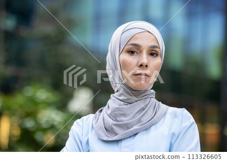 A modern Muslim woman wearing hijab stands confidently in an urban setting, exuding empowerment and diversity. 113326605