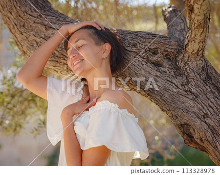 Beautiful Asian young woman in white dress outdoor near olive tree. embracing fresh air and engaging in outdoor activities. Friluftsliv concept means spending as much time outdoors as possible 113328978
