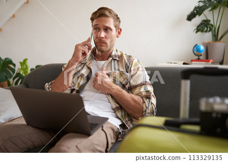 Portrait of man talking on mobile phone, tourist with laptop and suitcase answers telephone Portrait of man talking on mobile phone, tourist with laptop and suitcase answers telephone 113329135